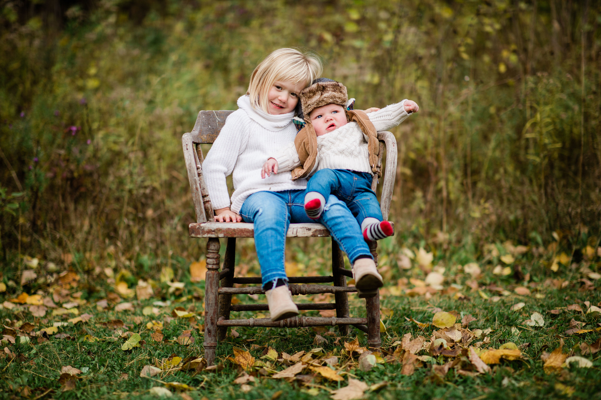Myra and Mackston in a meadow sitting on a vintage wooden chair.
