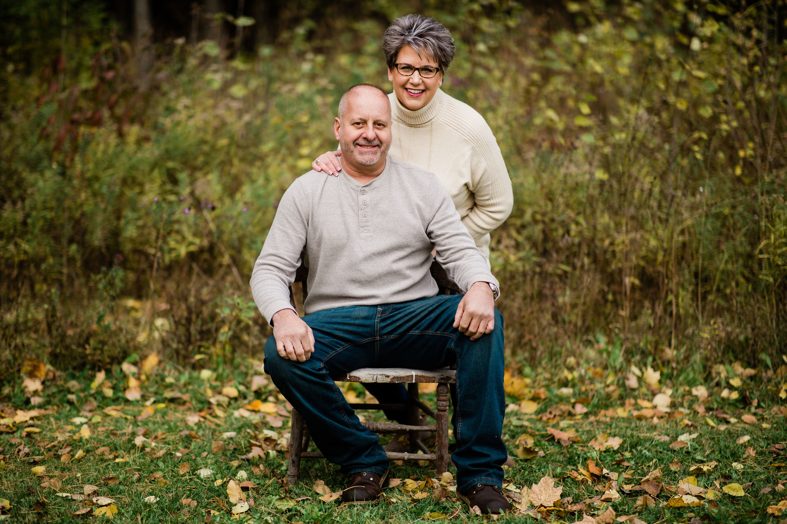 Dianne and Mark in a meadow sitting on a vintage wooden chair.