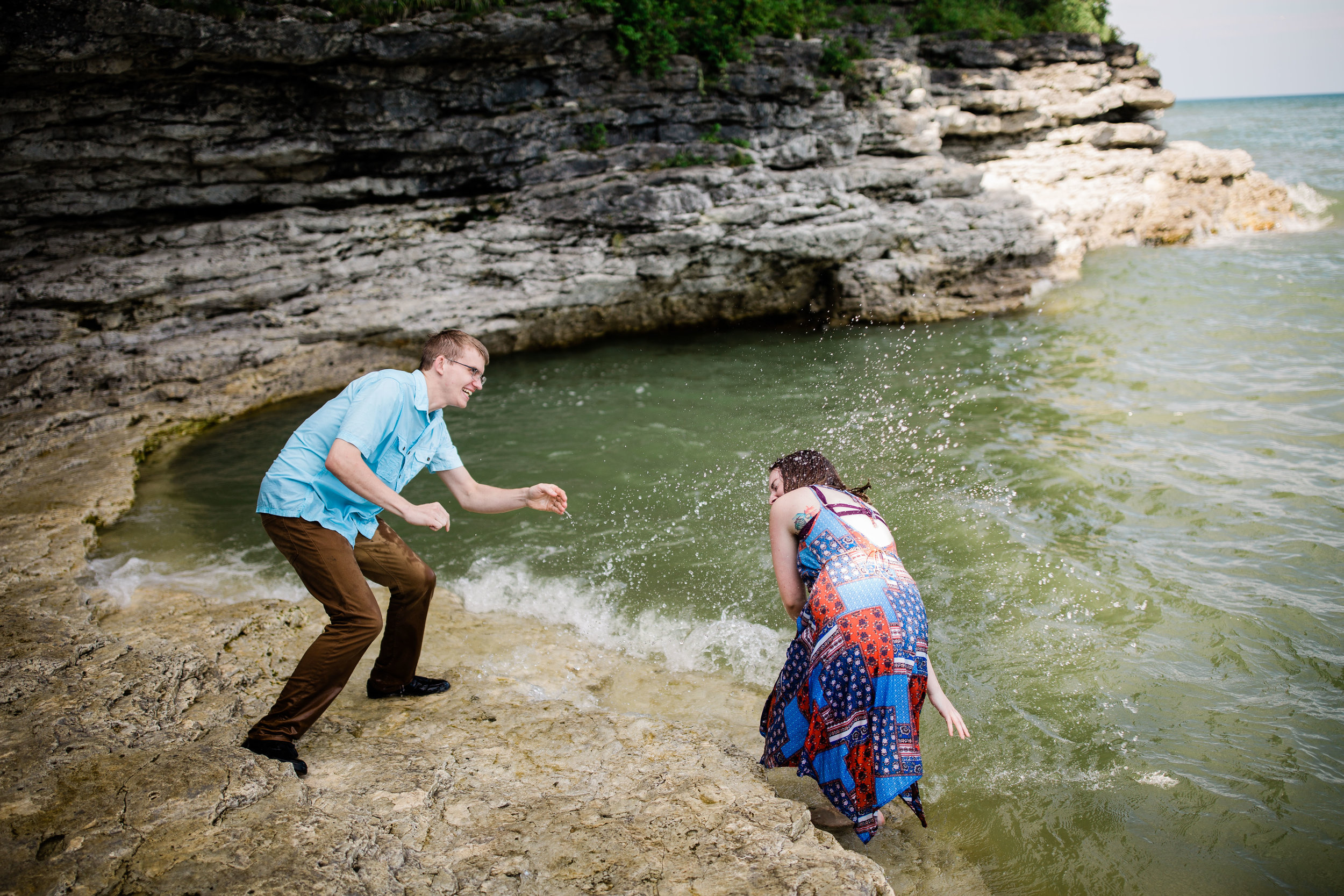 Ben and Lauren splashing each other on a rock beach at Cave Point County Park.