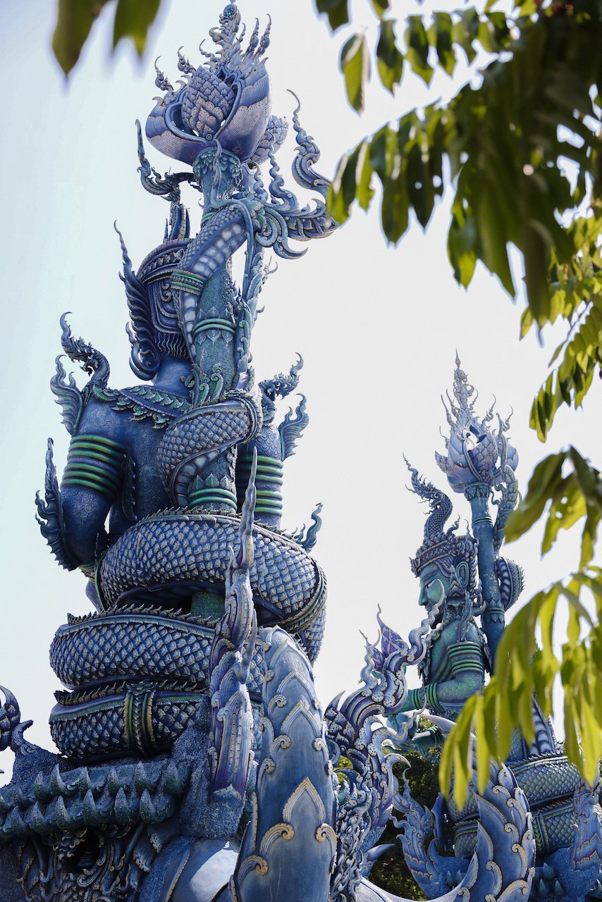 Two giant statues at the front with leaves - Blue Temple (Wat Rong Suea Ten) - Chiang Rai - Northern Thailand