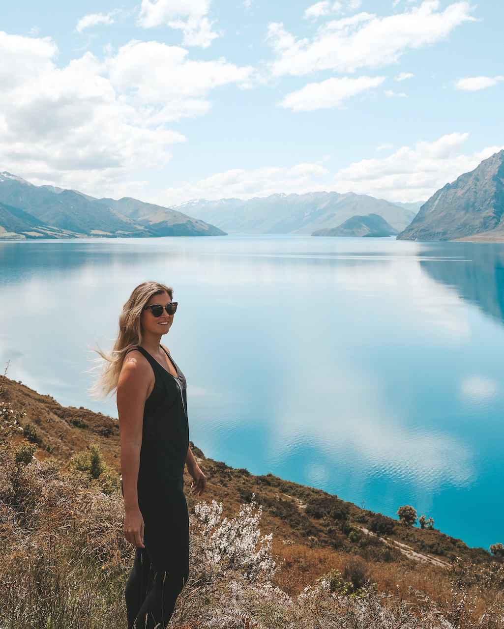 Woman posing in front of grandiose lake with mountain backdrop - Lake Hawea - New Zealand