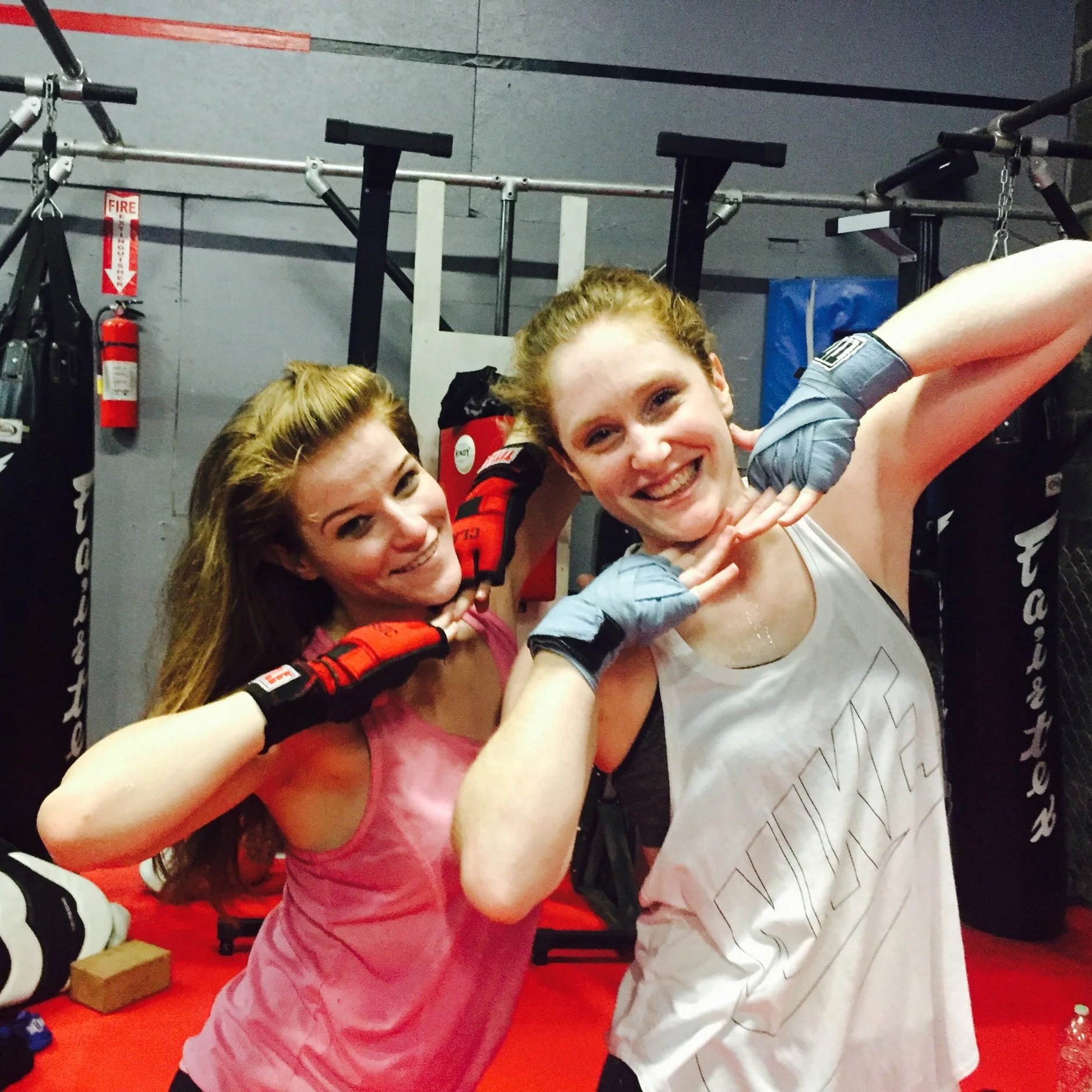 Two women in a gym, smiling and posing with boxing gloves, after a workout or training session.