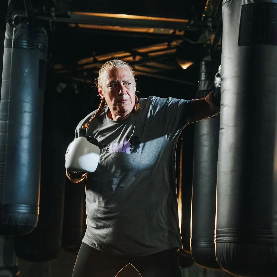 A woman practicing boxing with focus mitts in a gym surrounded by punching bags.