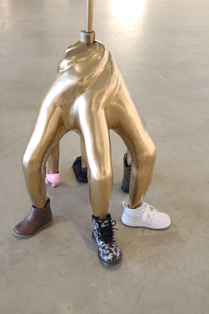 The different shoes on each of the sculpture's legs represent the variety of trendy styles parents might project onto their children: a cowboy boot, a pink patent leather heel, a Nike Air Jordan, a Chelsea boot, a Doc Marten boot, and a Yeezy Boost 350 sneaker. Each of these shoes has been miniaturized for children who have little or no idea about the various stereotypes placed on these shoes. My intention is to raise awareness about how children are bombarded with technology and consumerist ideals from a young age and to question how this might affect the development of future generations.