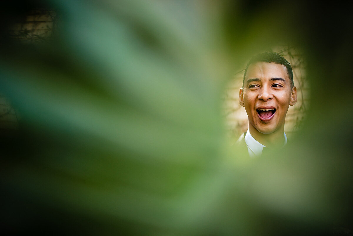 Funny reaction groom portrait shooting through a plant leaf.