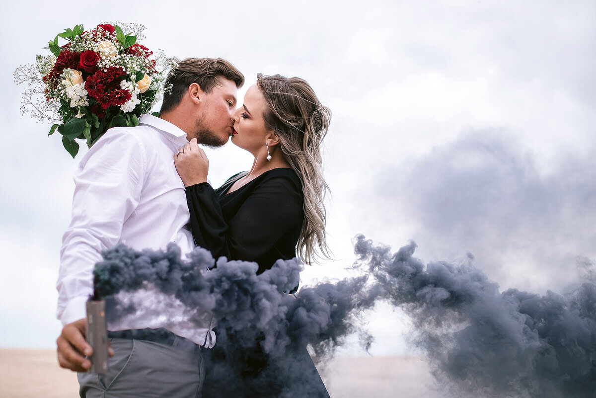 Engagement photos with black smoke bomb and black dress on the beach.