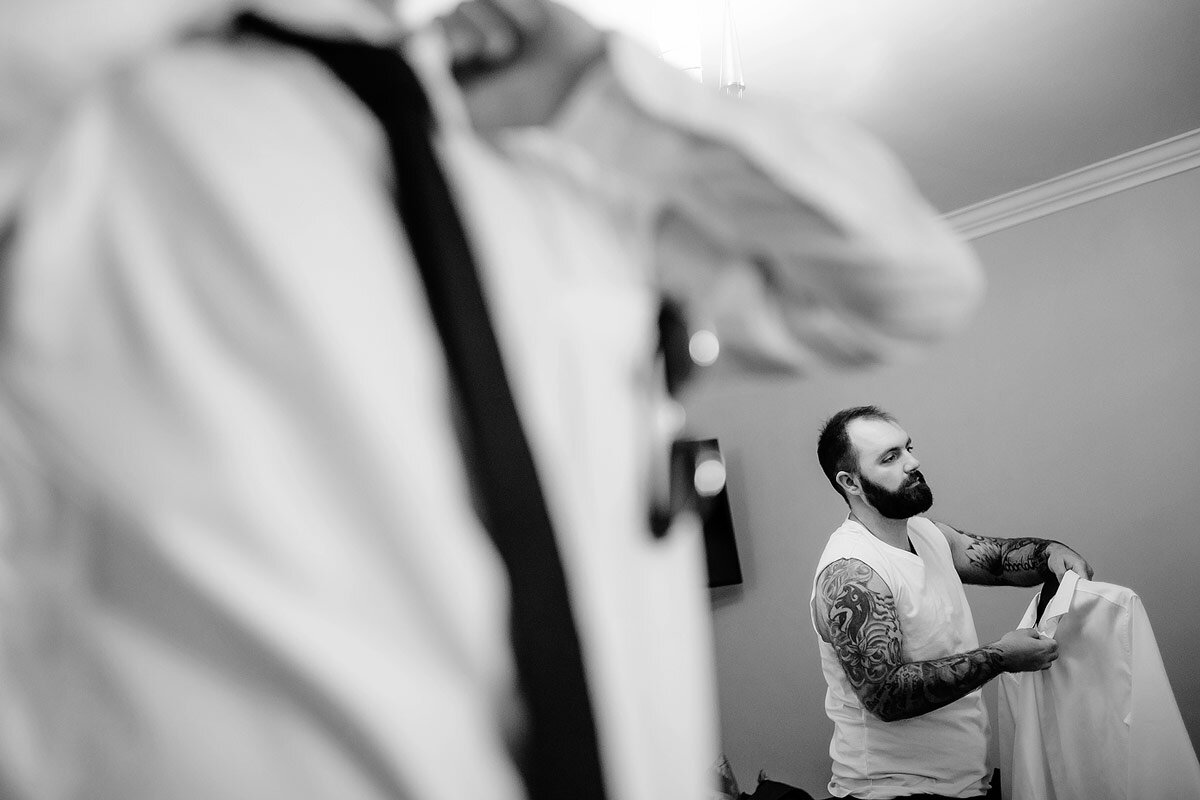 The groom with tattoos putting on his wedding shirt with groomsmen in the foreground.