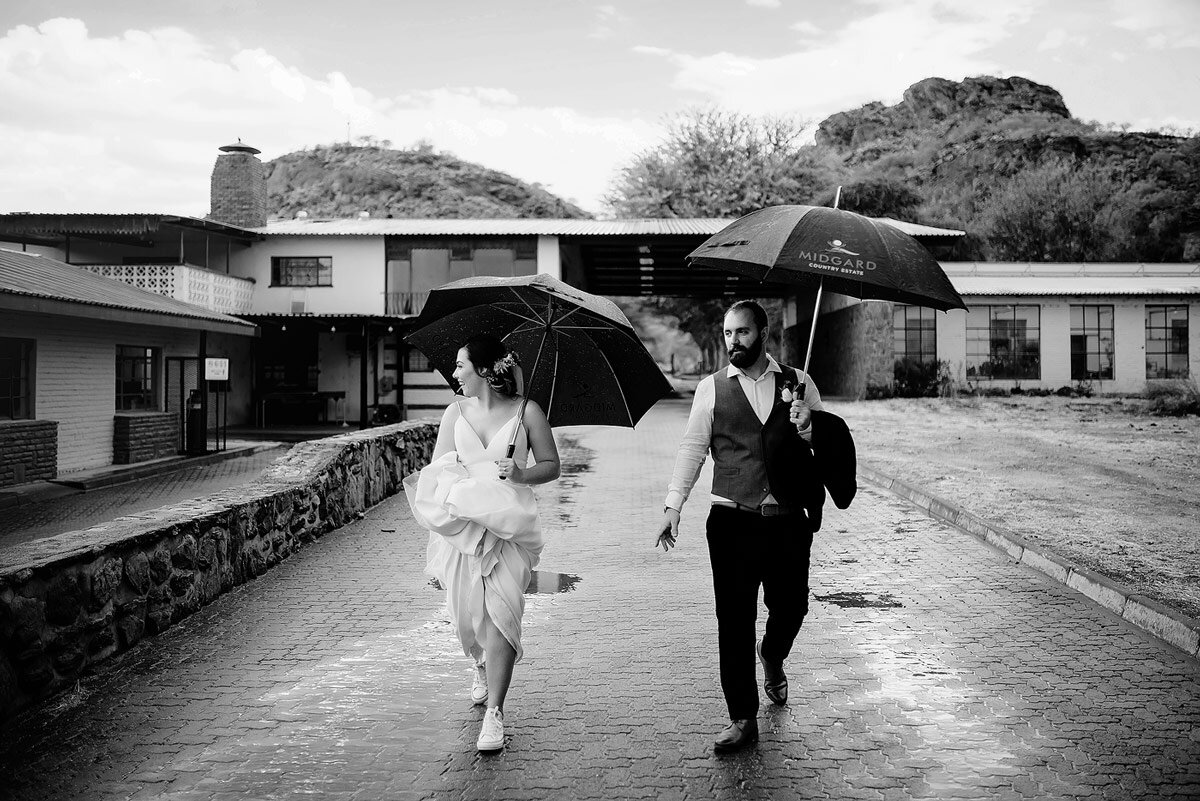 Wedding Rain as the couples walks at Midgard Estate in Namibia with umbrellas en route to their wedding couple photo shoot.