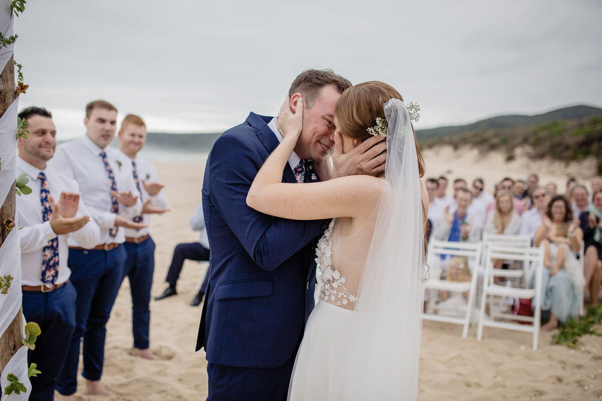 Wedding kiss with veil and guests on the beach in Plettenberg Bay South Africa. 