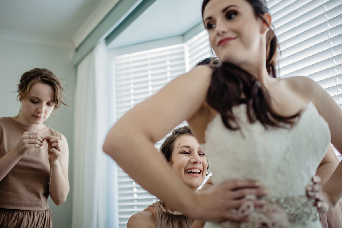 Bridesmaids helping the bride to put on her wedding dress before the wedding ceremony.