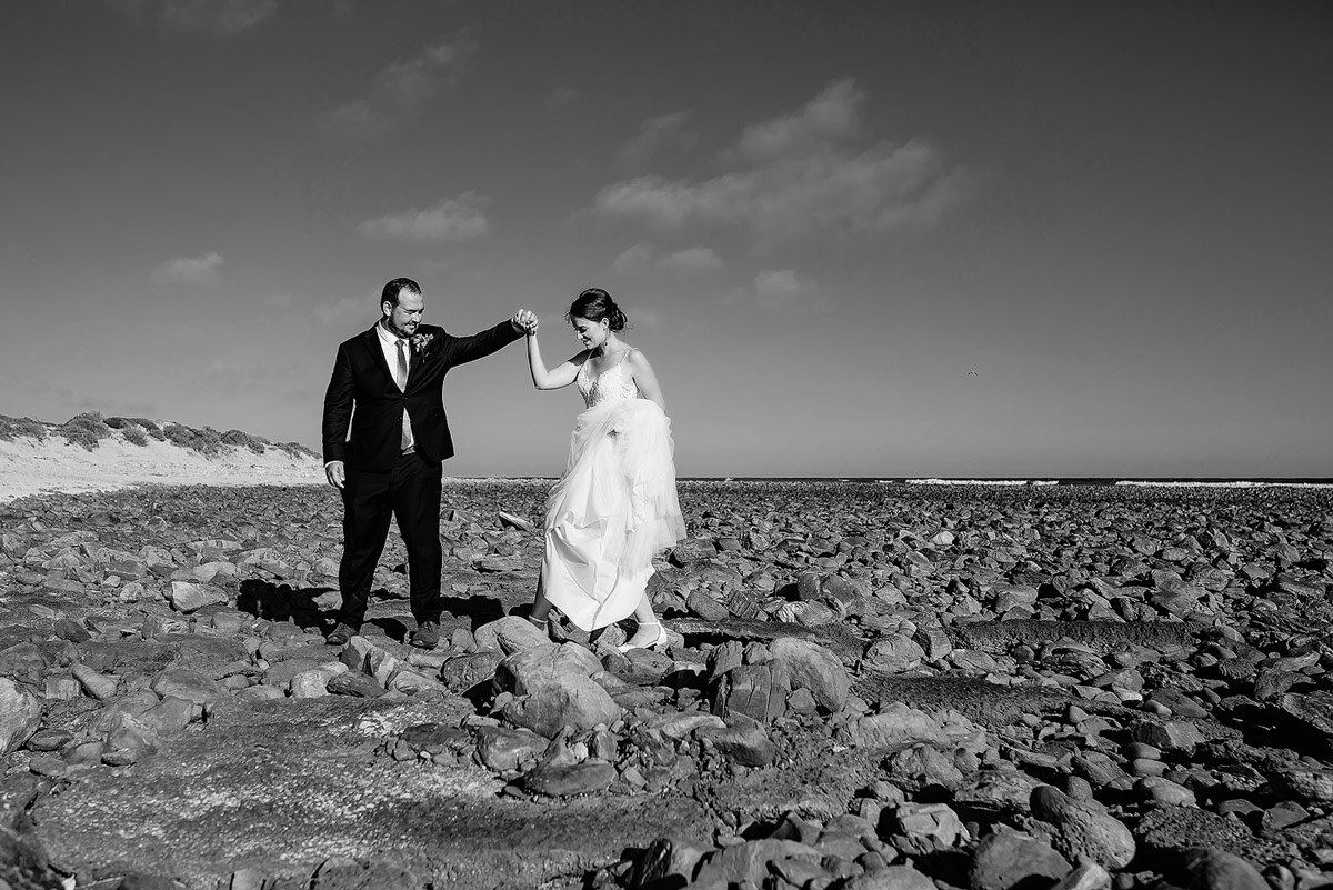 Bride and groom walking on a rocky beach at Gourikwa Reserve.