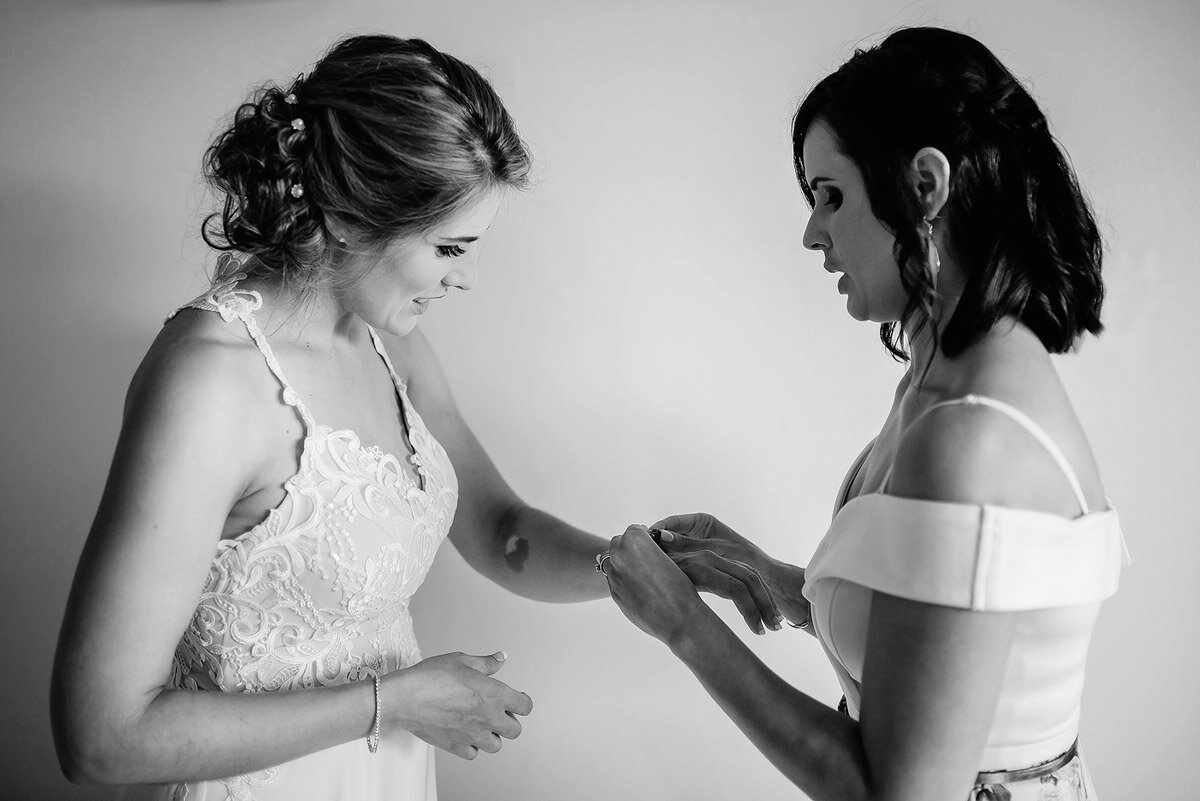 Bridesmaid helping her sister with wedding jewelry before the wedding ceremony.