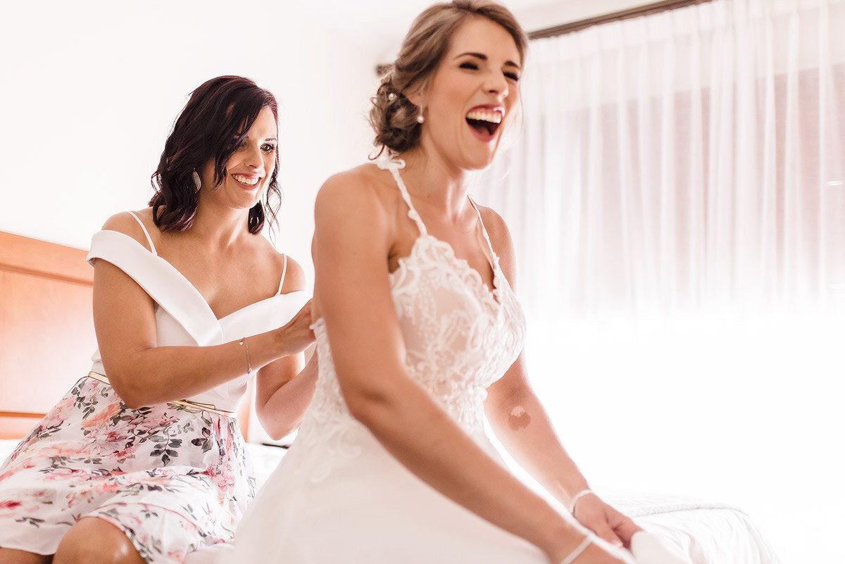 Funny moment between bride and bridesmaid while getting dressed at their wedding accommodation.