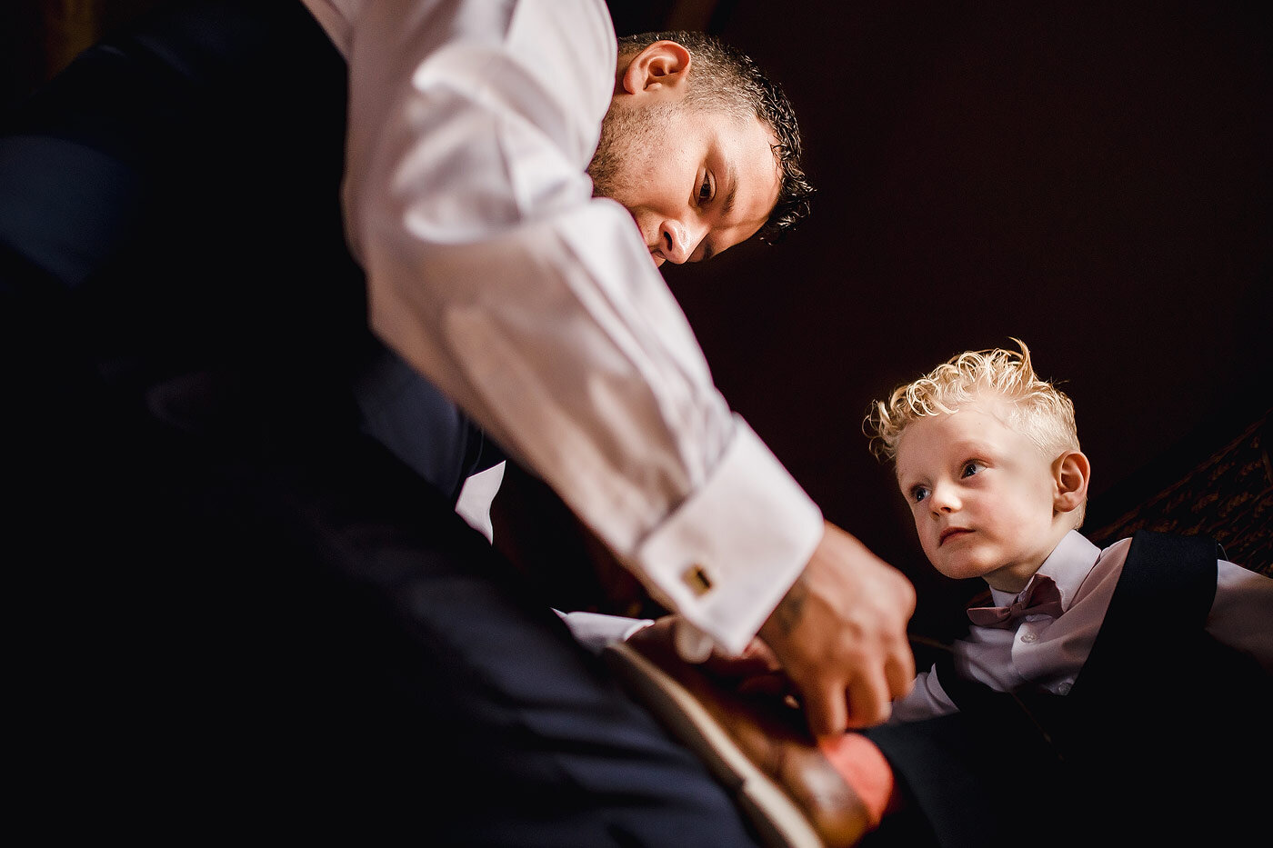 Ringbearer looking on as his shoes are tied.