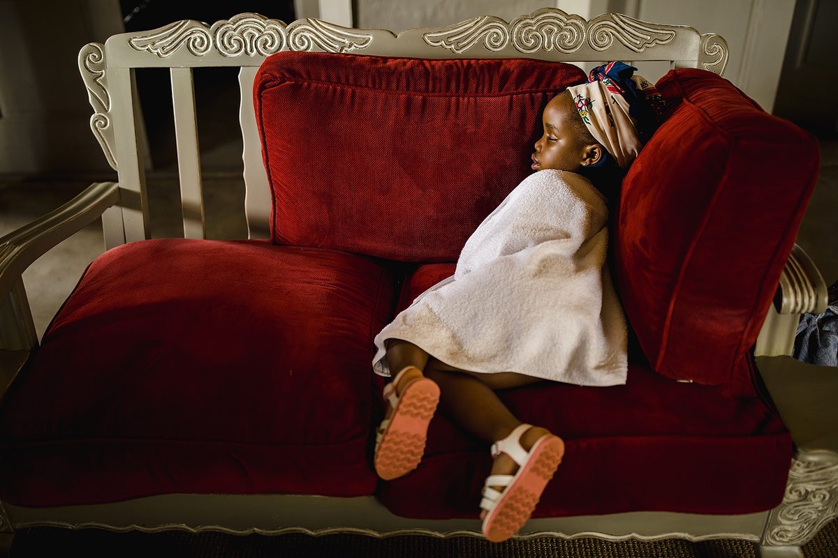 Flower girl sleeping on a red couch before the wedding.