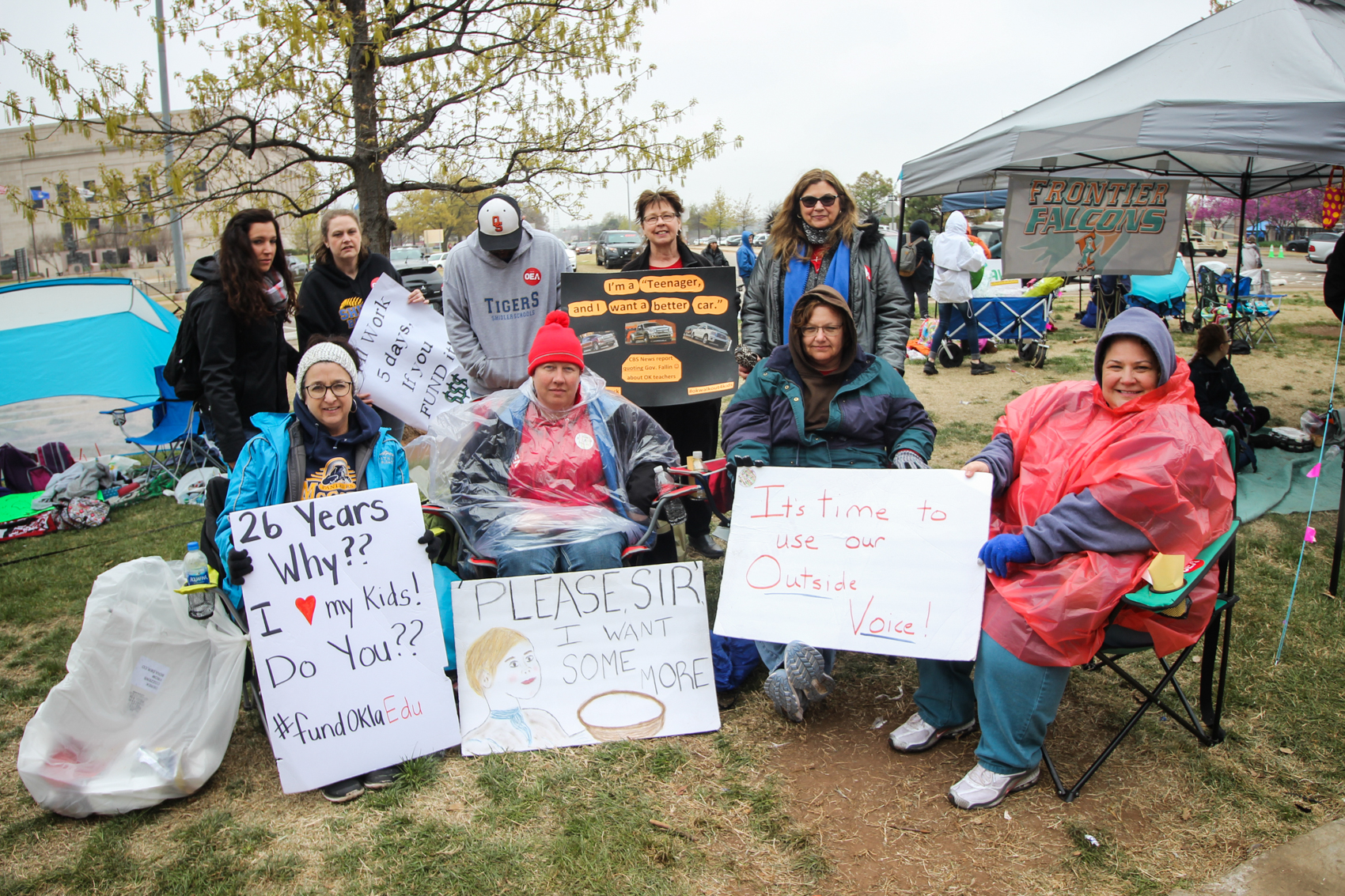 A group of teachers from Owasso County sit with their signs on the lawn of the Capitol building.