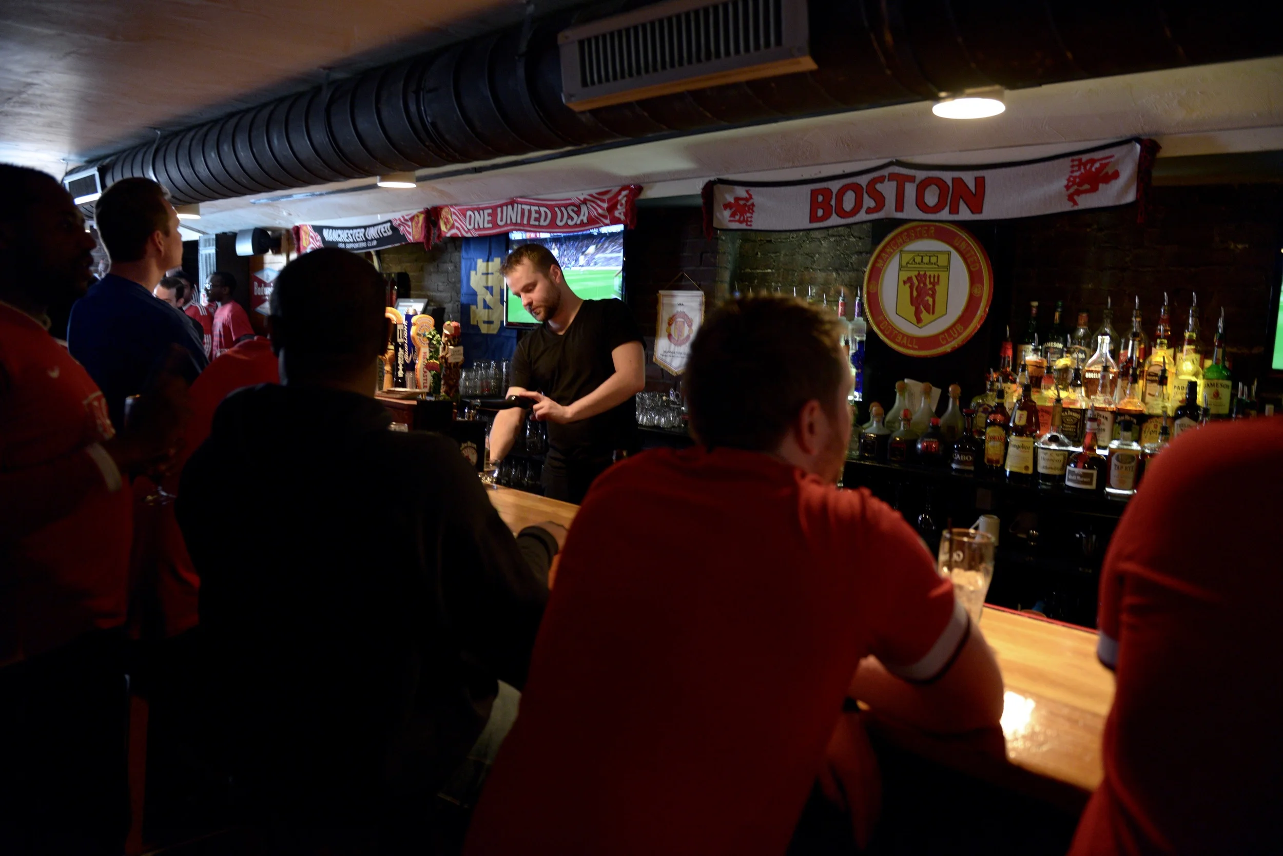 Televisions line both sides of the room. Some sit at the bar, while others gather in pockets around the screens.