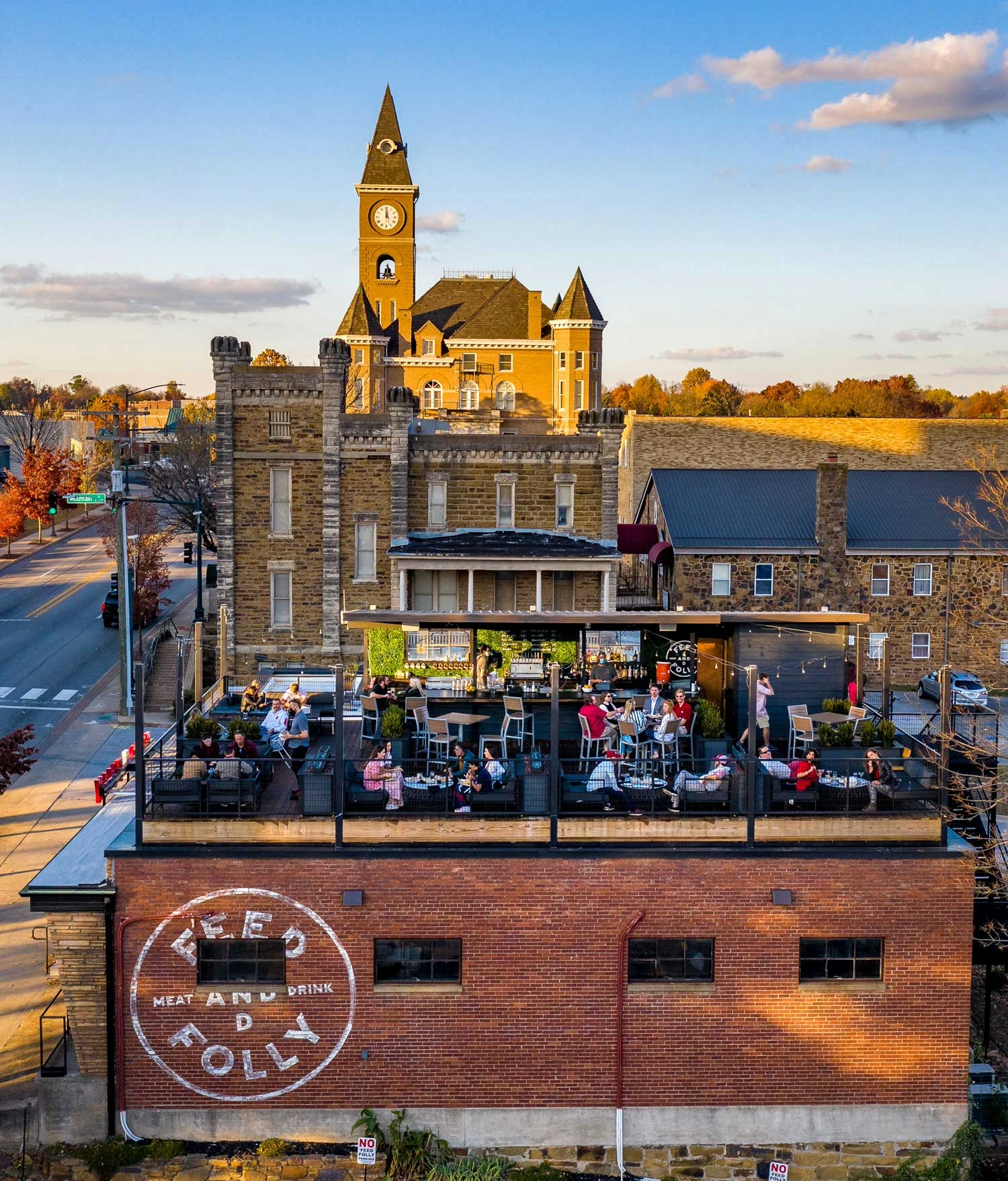 people sit at tables at a rooftop restaurant a historic building with clocktower is in the bacground