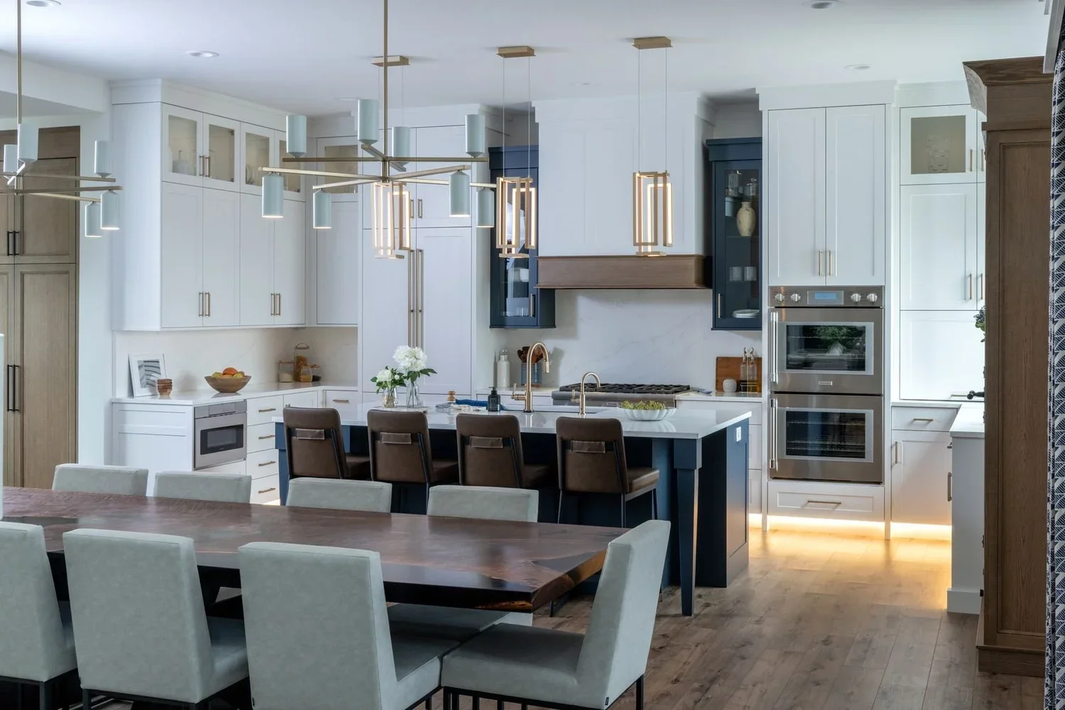 Luxury custom kitchen with navy island, double wall ovens, and live edge dining table in a Celebrity Builders home
