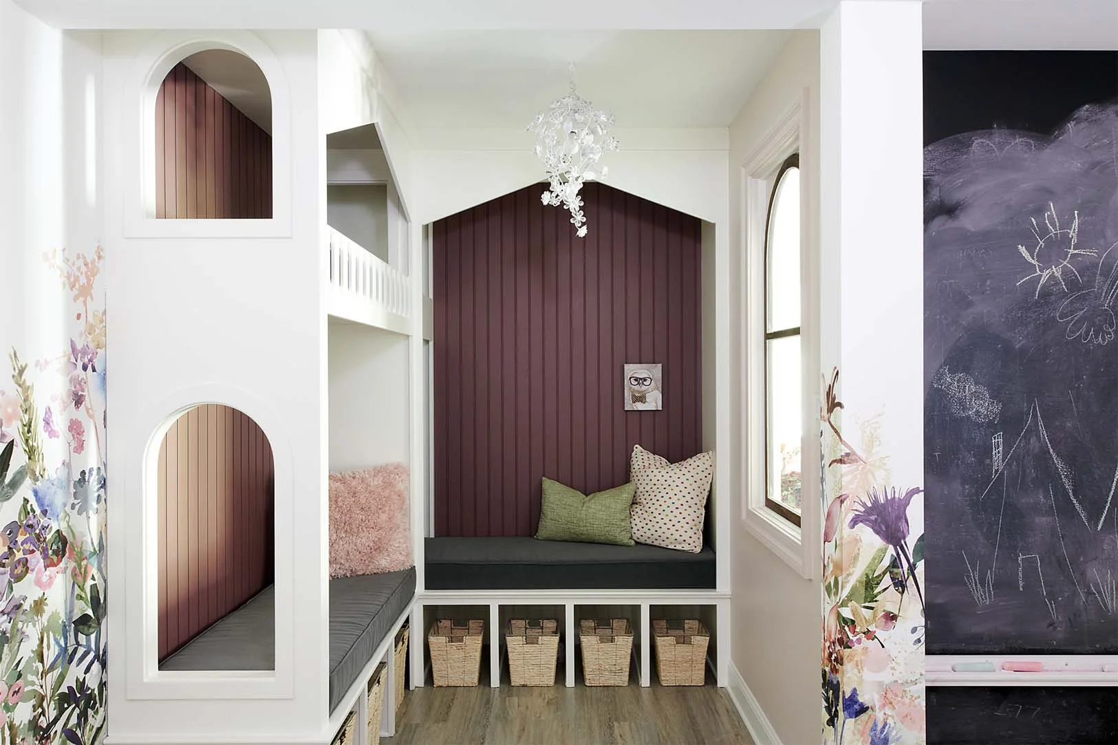 We turned an awkward nook in this L-shaped space into a fun playhouse daybed which makes for an ideal spot to read books together at night, or simply hang out with friends. Storage space under the playhouse to store stuffed animals, books, toys, etc, helps the space look clean and organized at the end of the day. The black chalkboard makes for a playful wall decoration and sits opposite a long art table where they can work on projects. Since there are no exterior walls in the space, we added a repurposed window in the playhouse nook to bring in natural light from the main living area of the lower level. The white neutral base color keeps the look mature for when the girls get older.