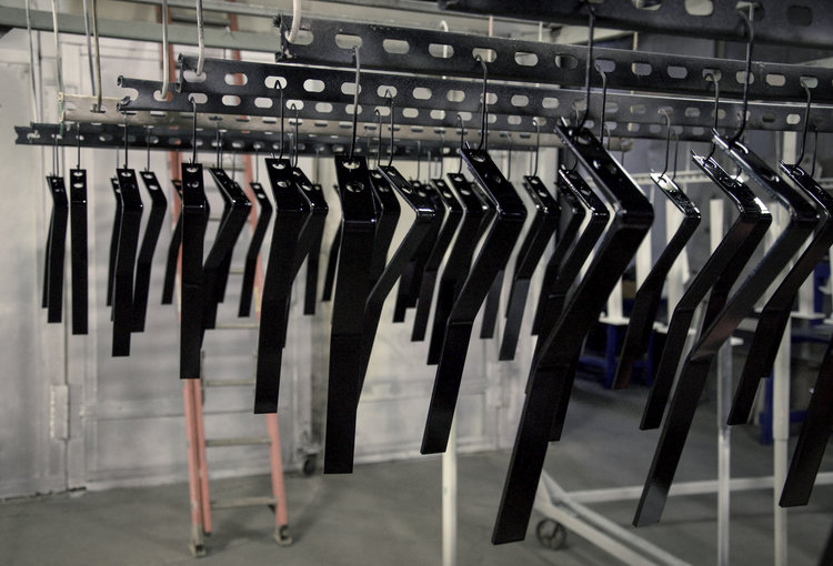 L-shaped metal pieces painted shiny black and suspended to dry.