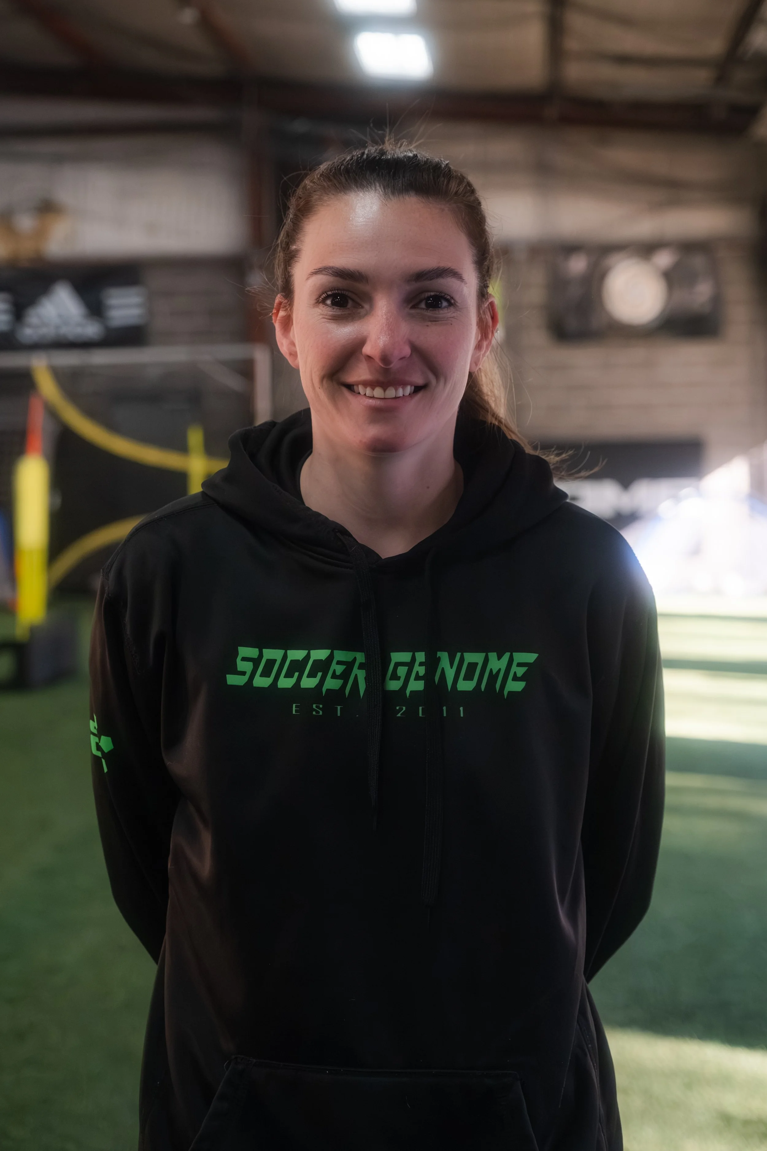 Person wearing a black hoodie with "Soccer Genome Est. 2011" text, standing indoors on a sport field.