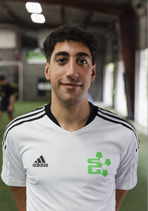 Soccer player in a white and black jersey with an Adidas logo, standing on an indoor soccer field.