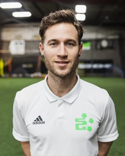 A smiling man in a white Adidas polo shirt standing in an indoor sports facility.