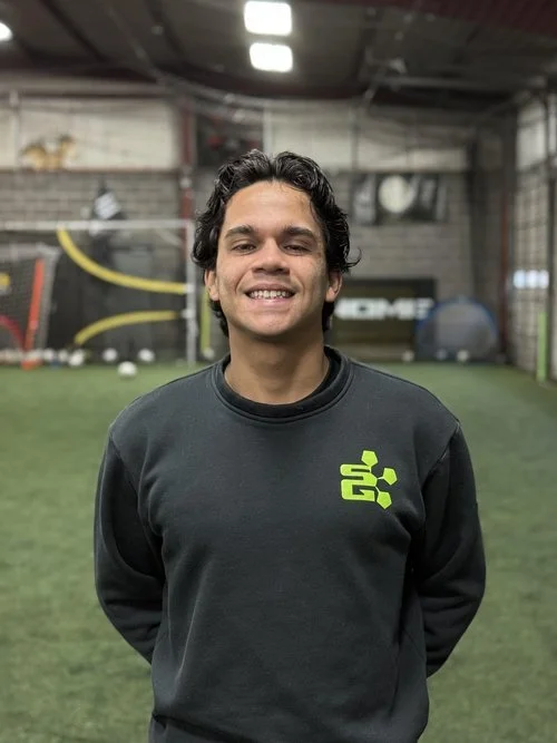 Smiling person in a sports facility wearing a dark sweatshirt with logo.