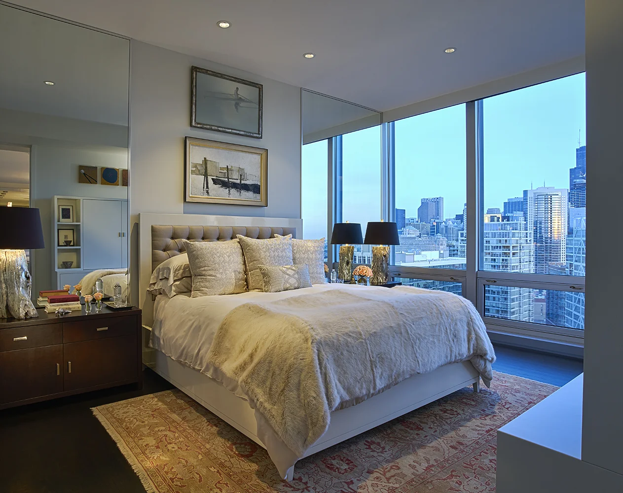 A custom lacquered bed with sustainable bamboo bedding sits atop an antique carpet. Mirrors on either side of the bed create a greater sense of height and depth to the room.