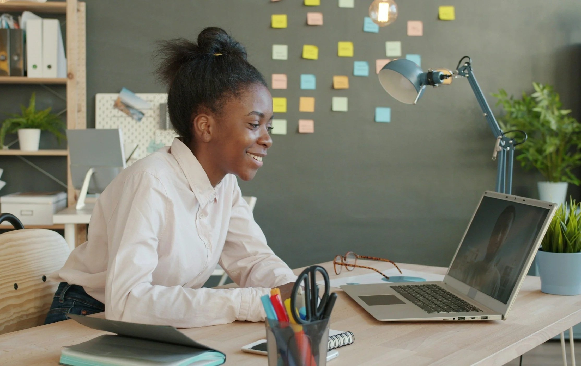 woman on a virtual in-depth interview with a man on the computer, in an office with sticky notes on the wall in the background.