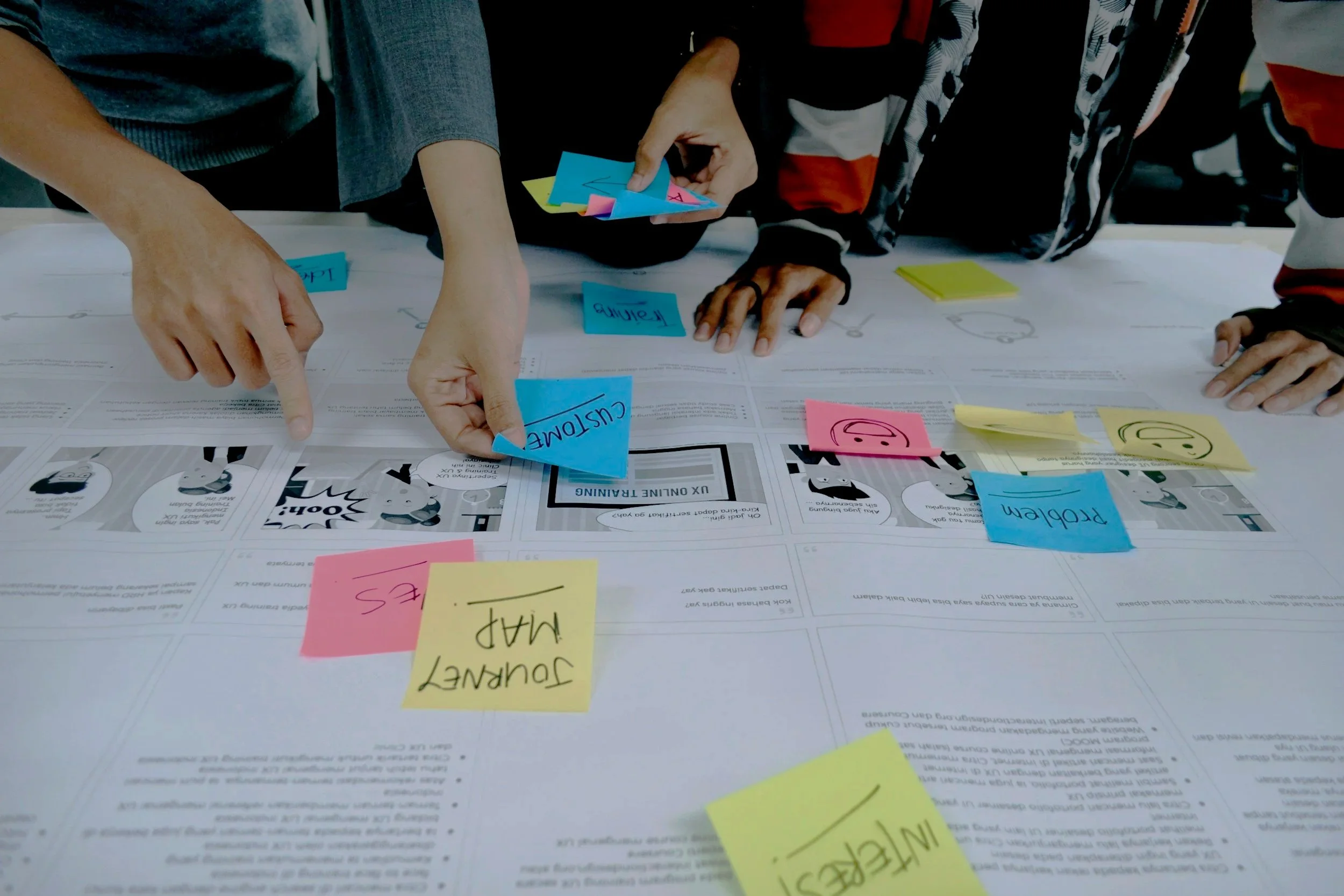 People collaborating at a table with colorful sticky notes and printed documents, engaging in a brainstorming session.