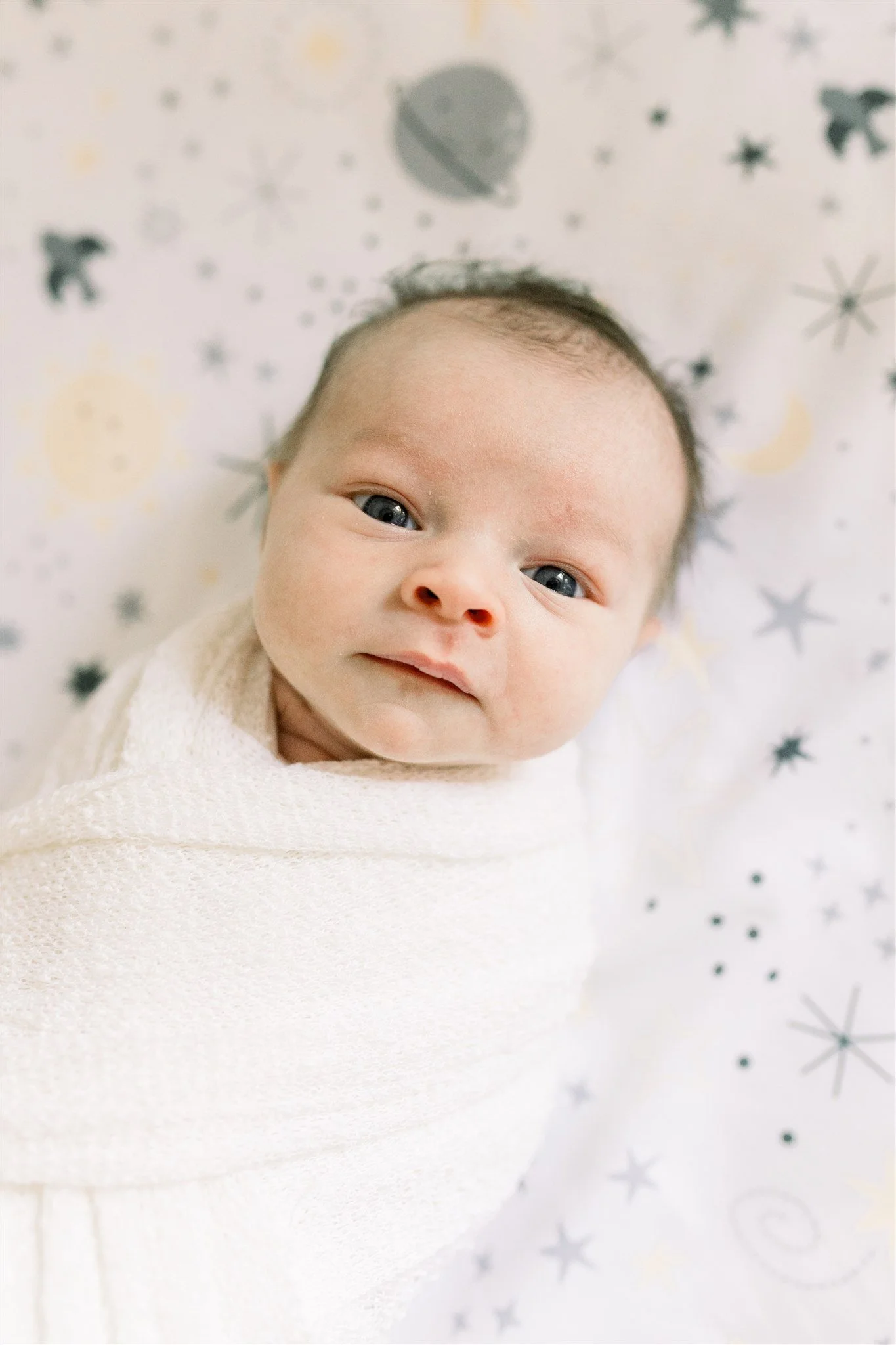 Wide eyed baby girl looking up while laying down in crib on star sheets