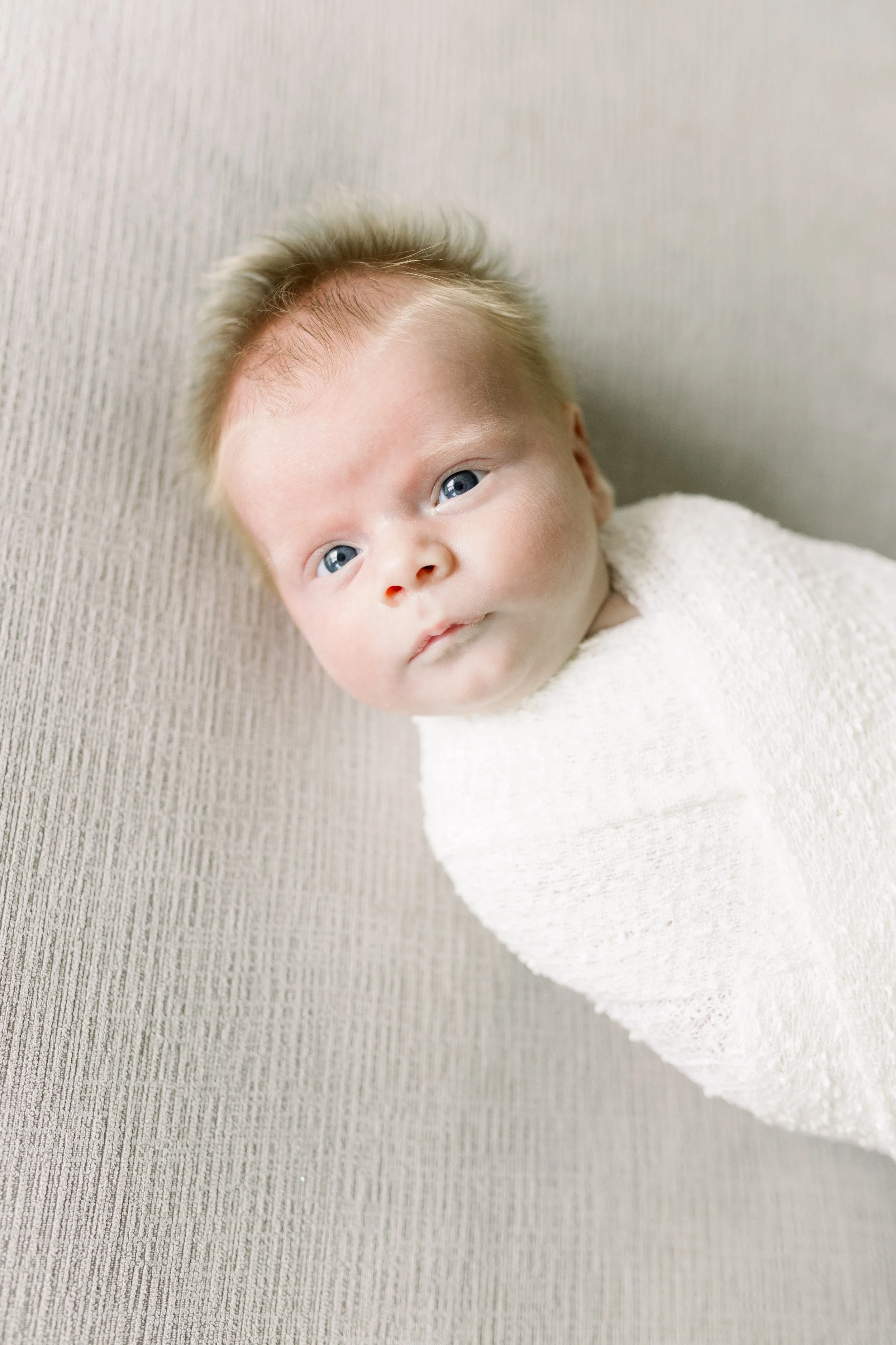 Blonde baby wide eyed on bed swaddled