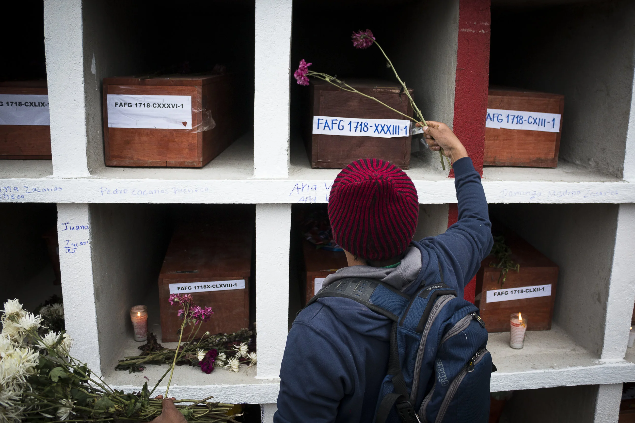 Un joven coloca flores sobre las cajas que contienen los restos de las victimas.