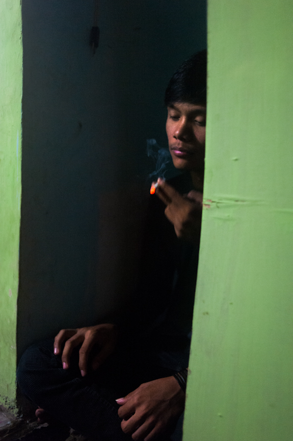 Rheza takes a drag from his friend Aif's clove cigarette while sitting in the mushollah, prayer room, of the Rayon during a discussion.