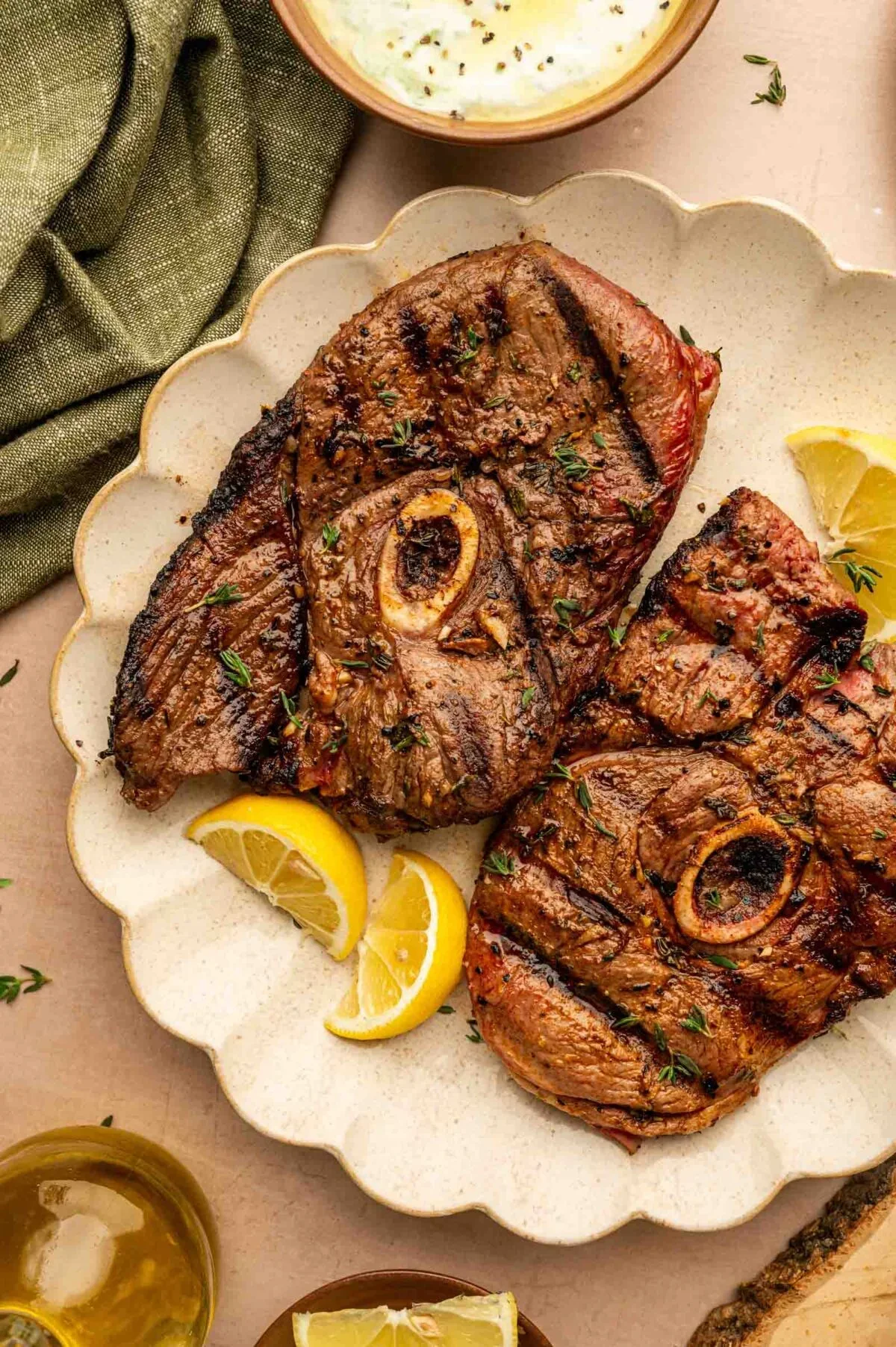 Grilled lamb leg steaks on a white decorative plate with lemon wedges.