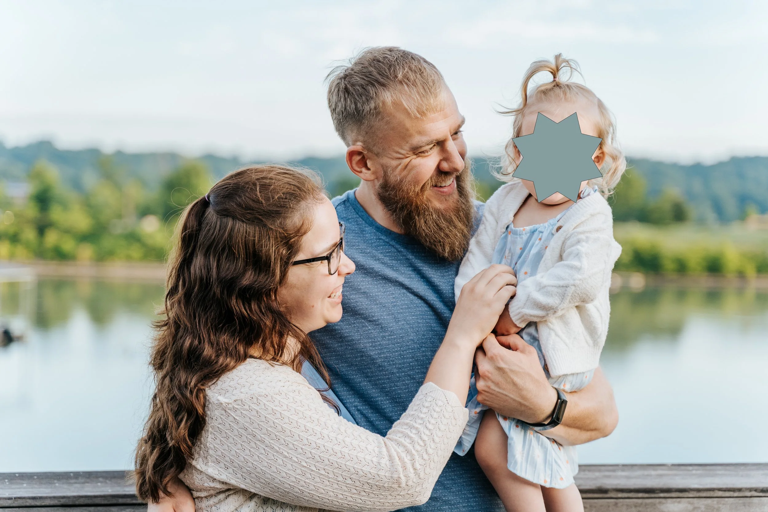 Dad holds toddler daughter while Mom tickles her belly to make her giggle.