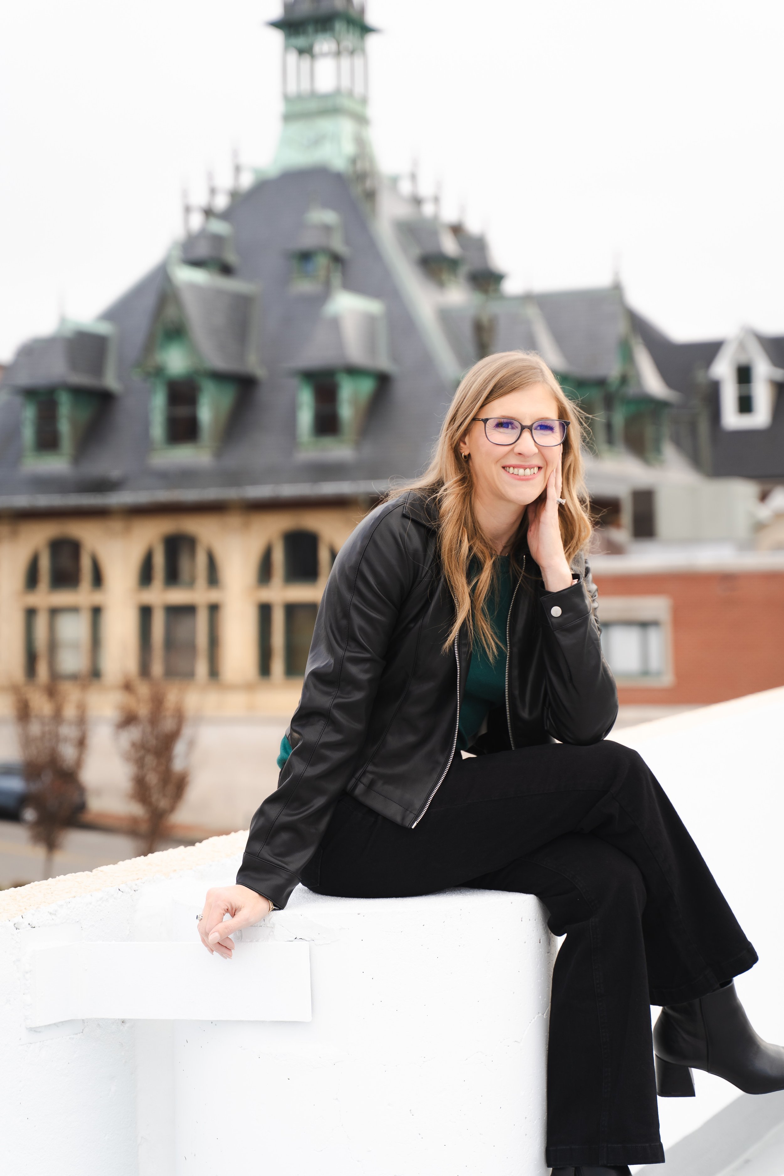 Business woman sits on the edge of a wall with Clarksville's Customs House Museum behind her.