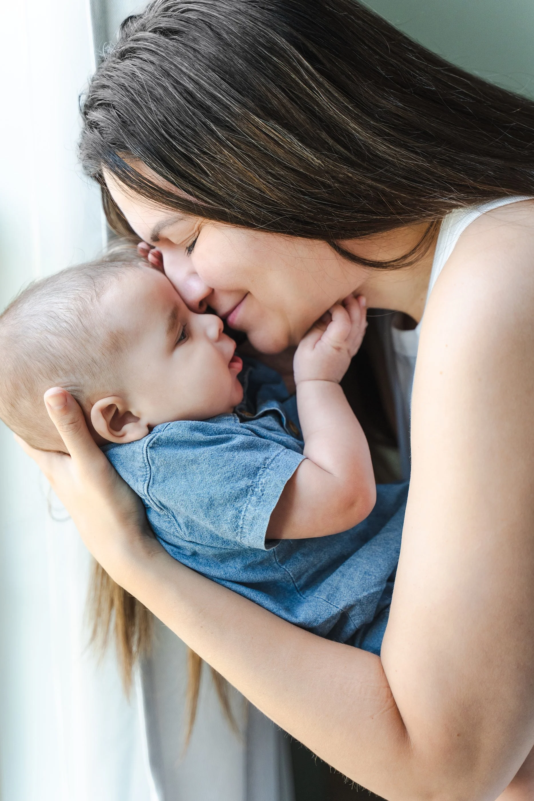 New mom snuggles her face against her baby boy while he gently touches her chin in their Clarksville, TN home..
