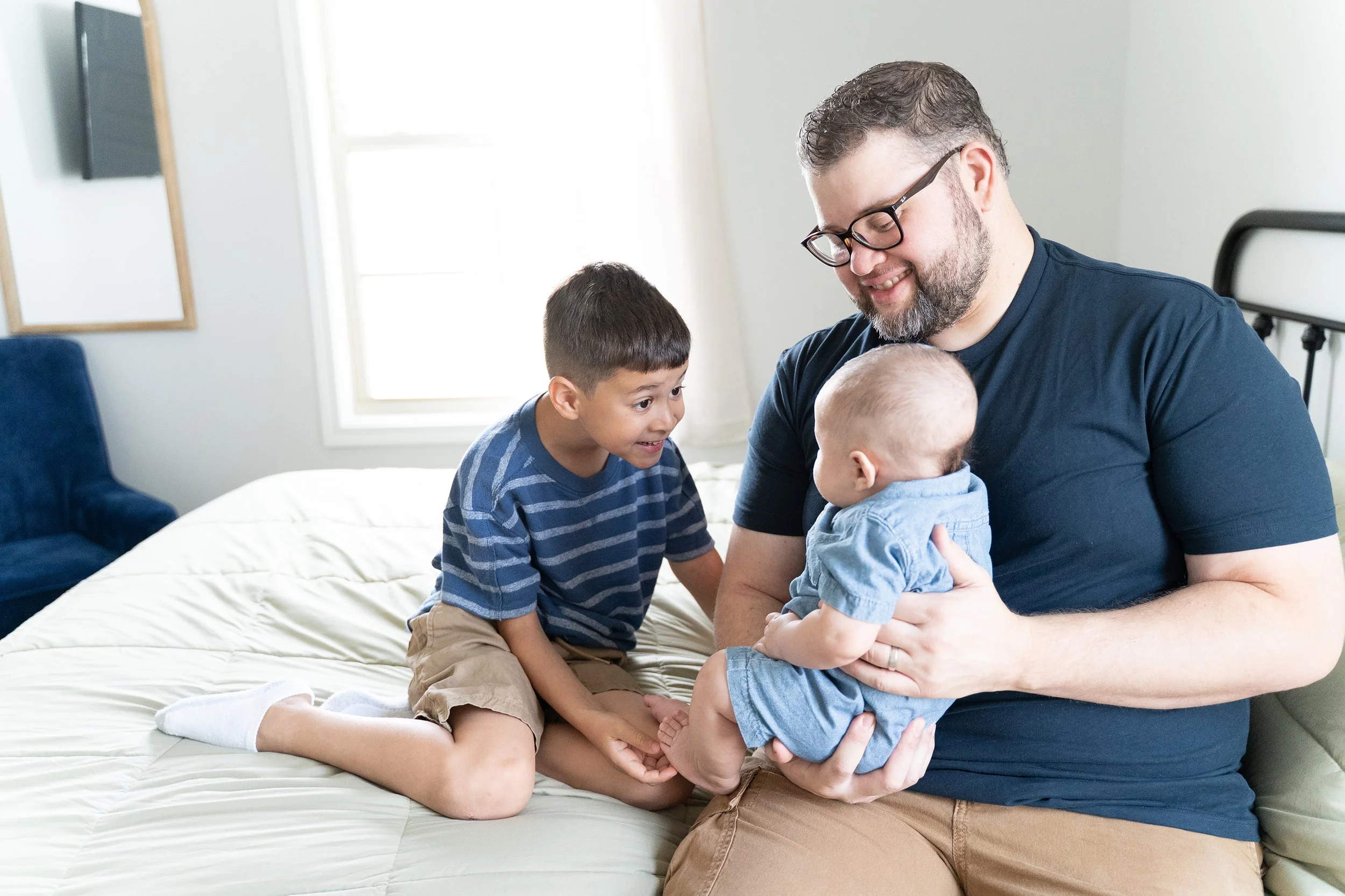 Father holds new baby boy while his brother tickles his feet to try and make him laugh during Clarksville newborn photo session.