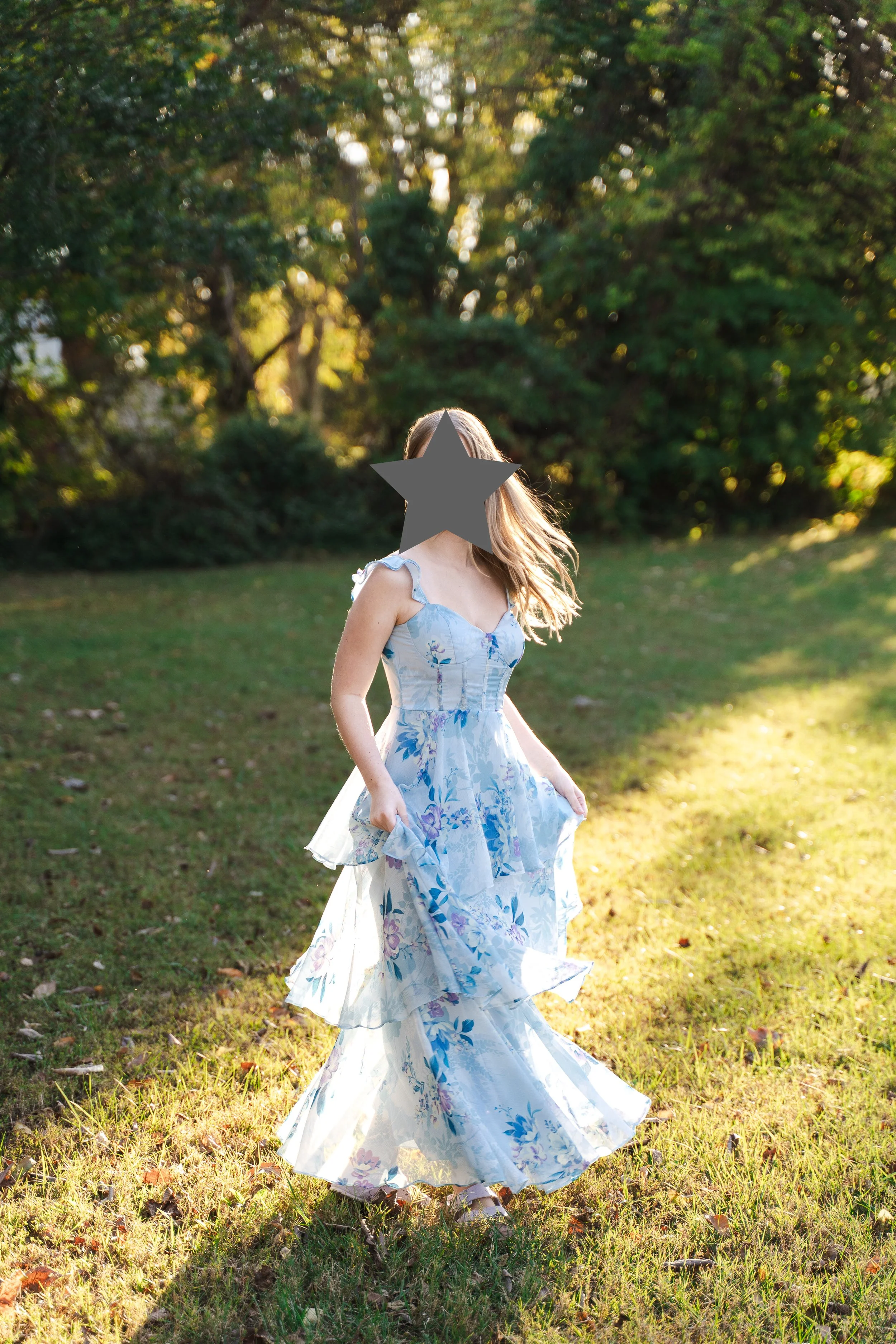 A backlit full length portrait of a high school senior spinning in a blue dress.