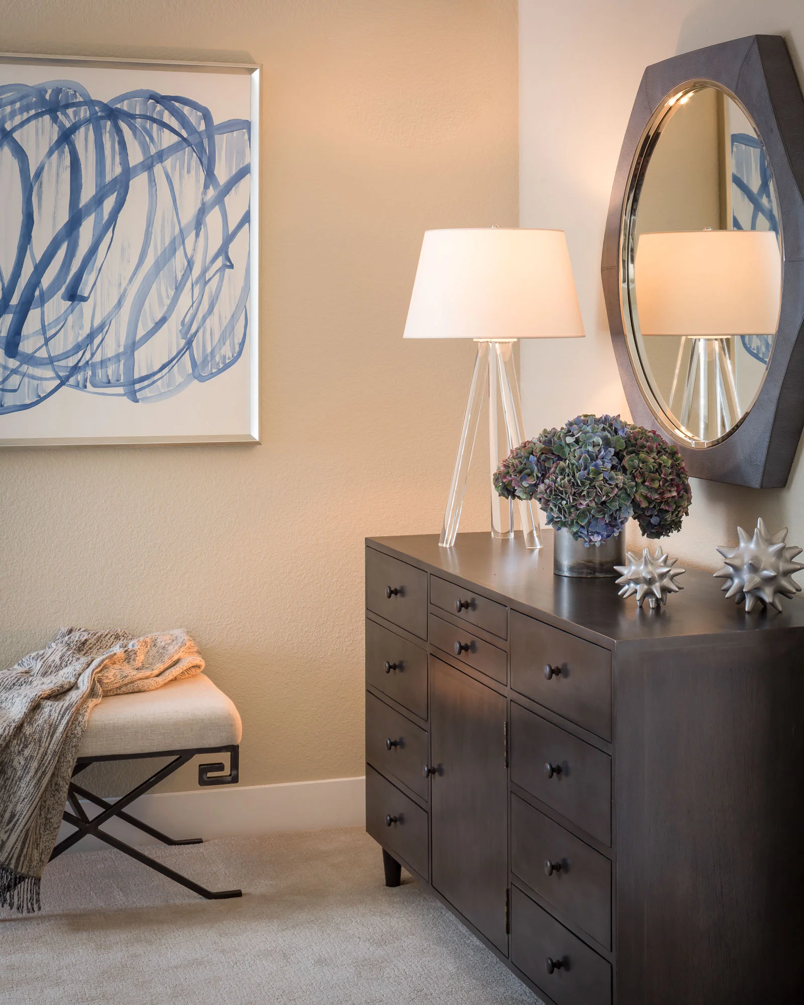 Danville, CA masculine Master Bedroom with a grey-finish wooden dresser, grey hexagon mirror, bench with throw and blue and white art