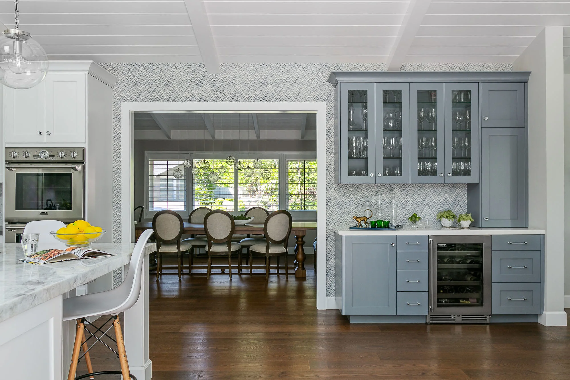Danville, CA kitchen with built-in blue bar and wine refrigerator, Nautical Navy Holland & Sherry wallpaper looking into the dining room with custom Shakuff orb light fixtures.