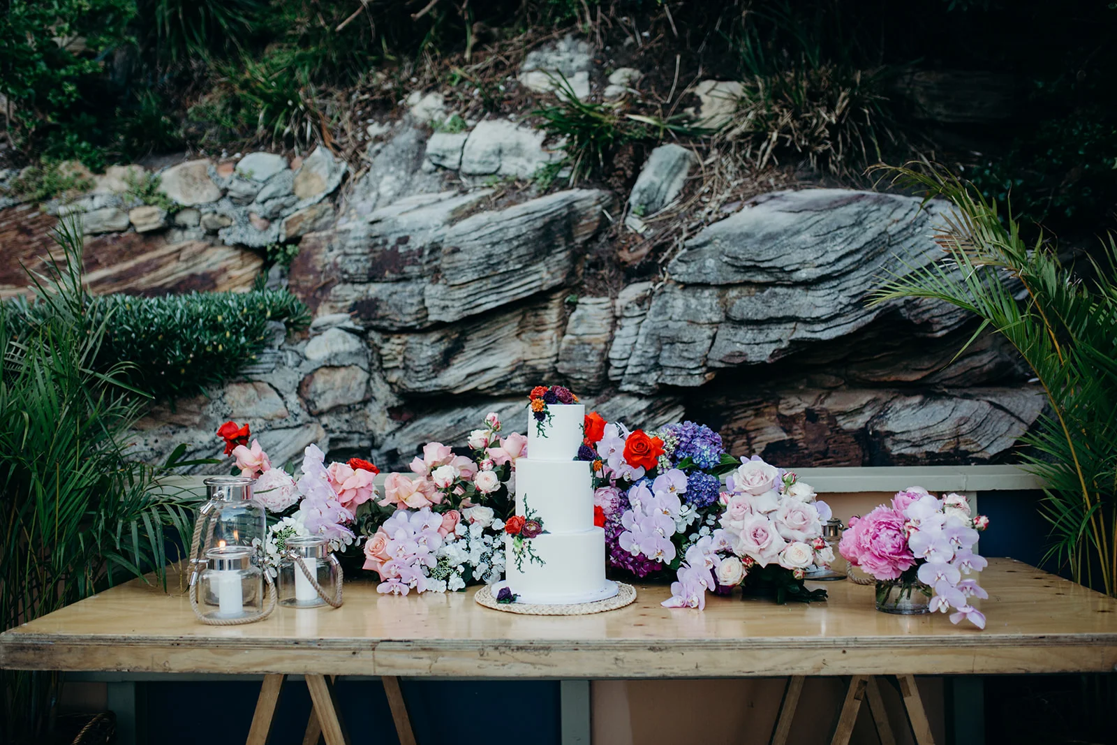 The cake! Featuring jewel toned buttercream flowers over crisp white icing. All vegan!! Surrounded by a floral garden. Image by Folk & Follow