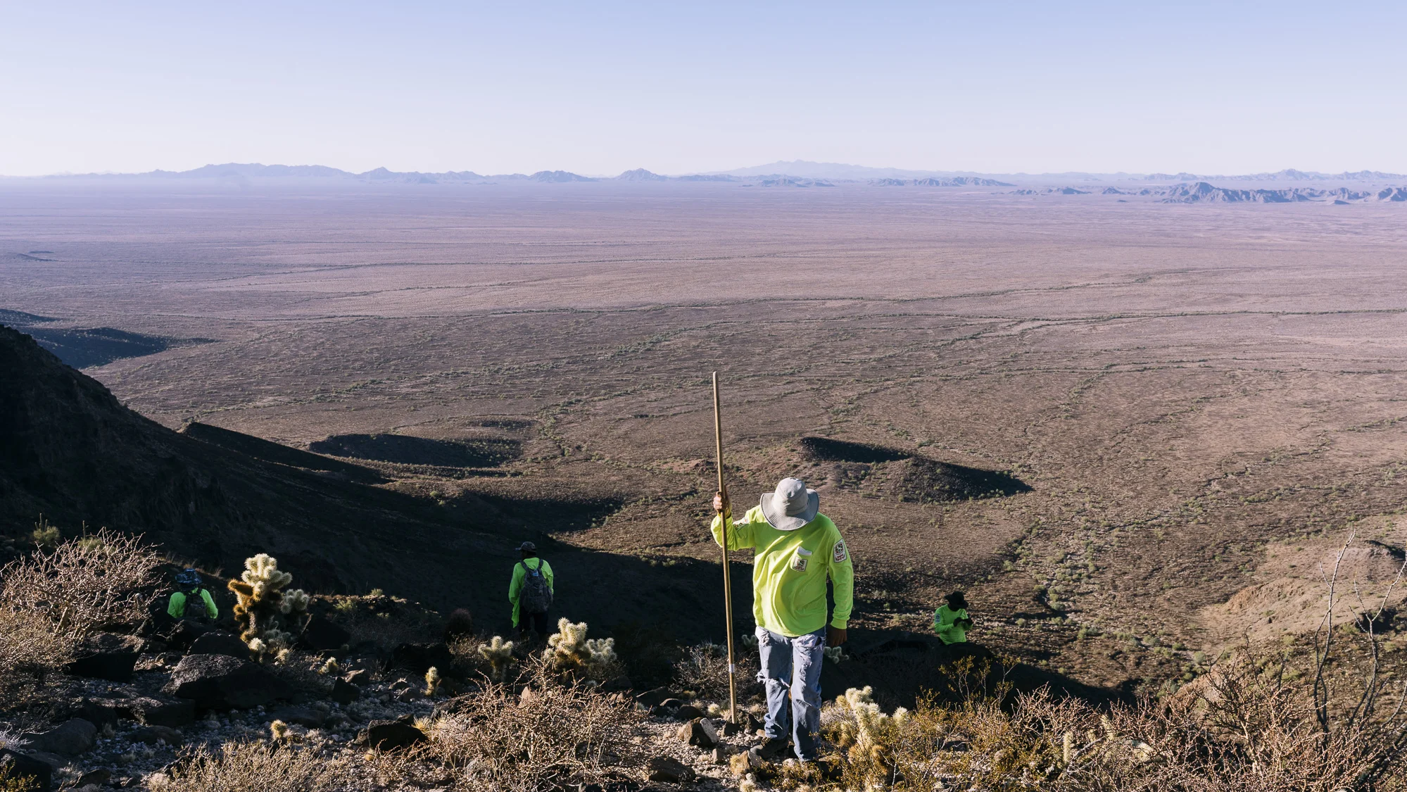 IMAGE CAPTION: Volunteers from Aguilas Del Desierto scour a mountain peak above the Barry M. Goldwater Air Force Range. Passage through the active firing range, where pilots practice air-to-ground bombing, rocket delivery, and strafing, is the final gauntlet for migrants before reaching Interstate 8, where their guides will have arranged a vehicle pickup.