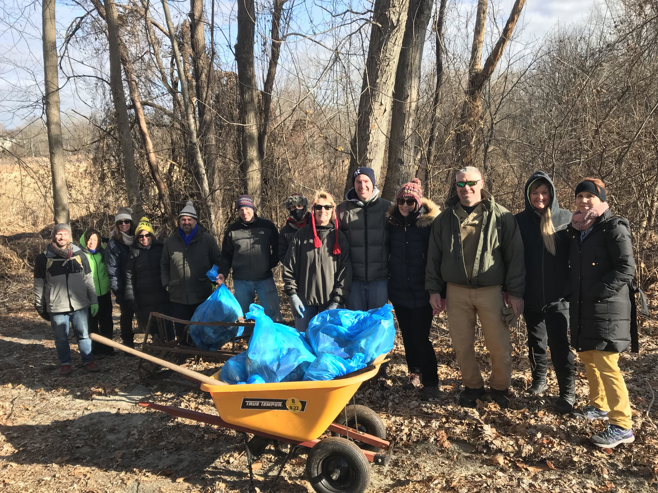  group volunteer photo with a yellow wheel barrow in front and bright blue trash bags piled inside 