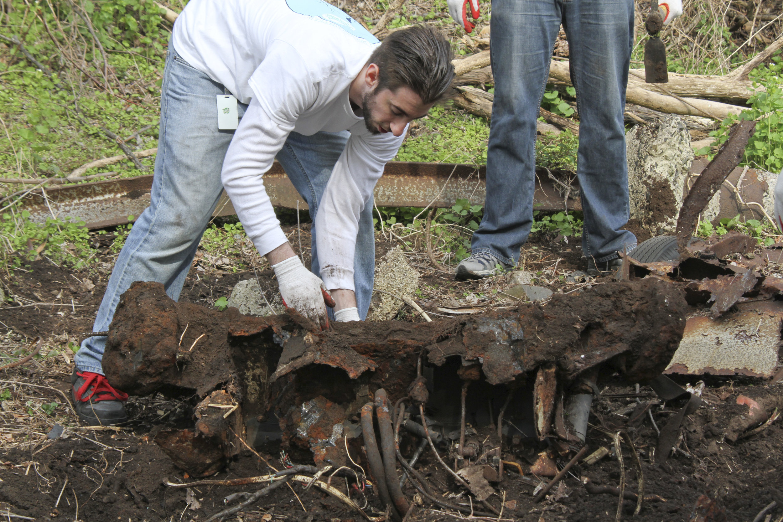  a volunteer works to lift heavy metal debris while someone looks on 