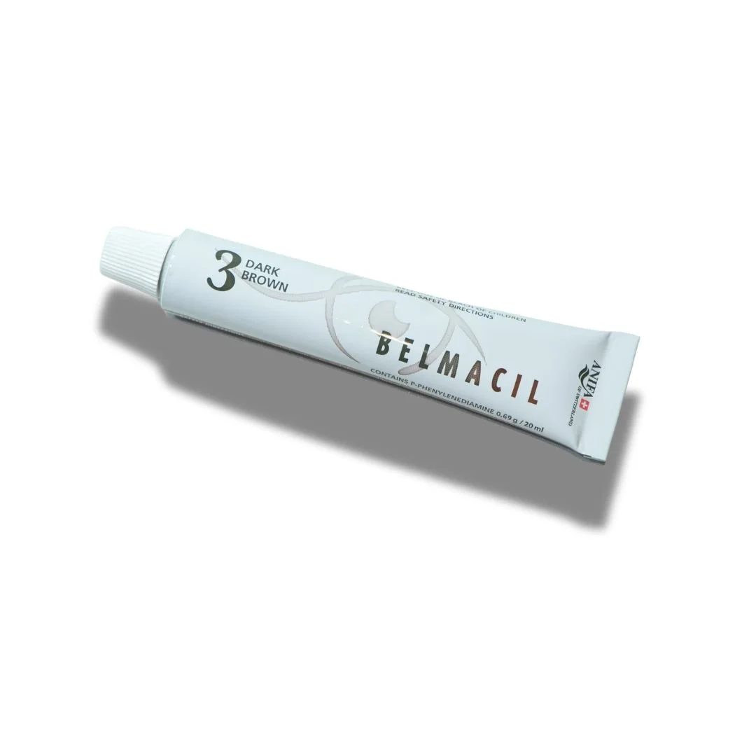 A tube of Belmacil lash and brow tint in dark brown, lying on a white surface with a shadow beneath it.