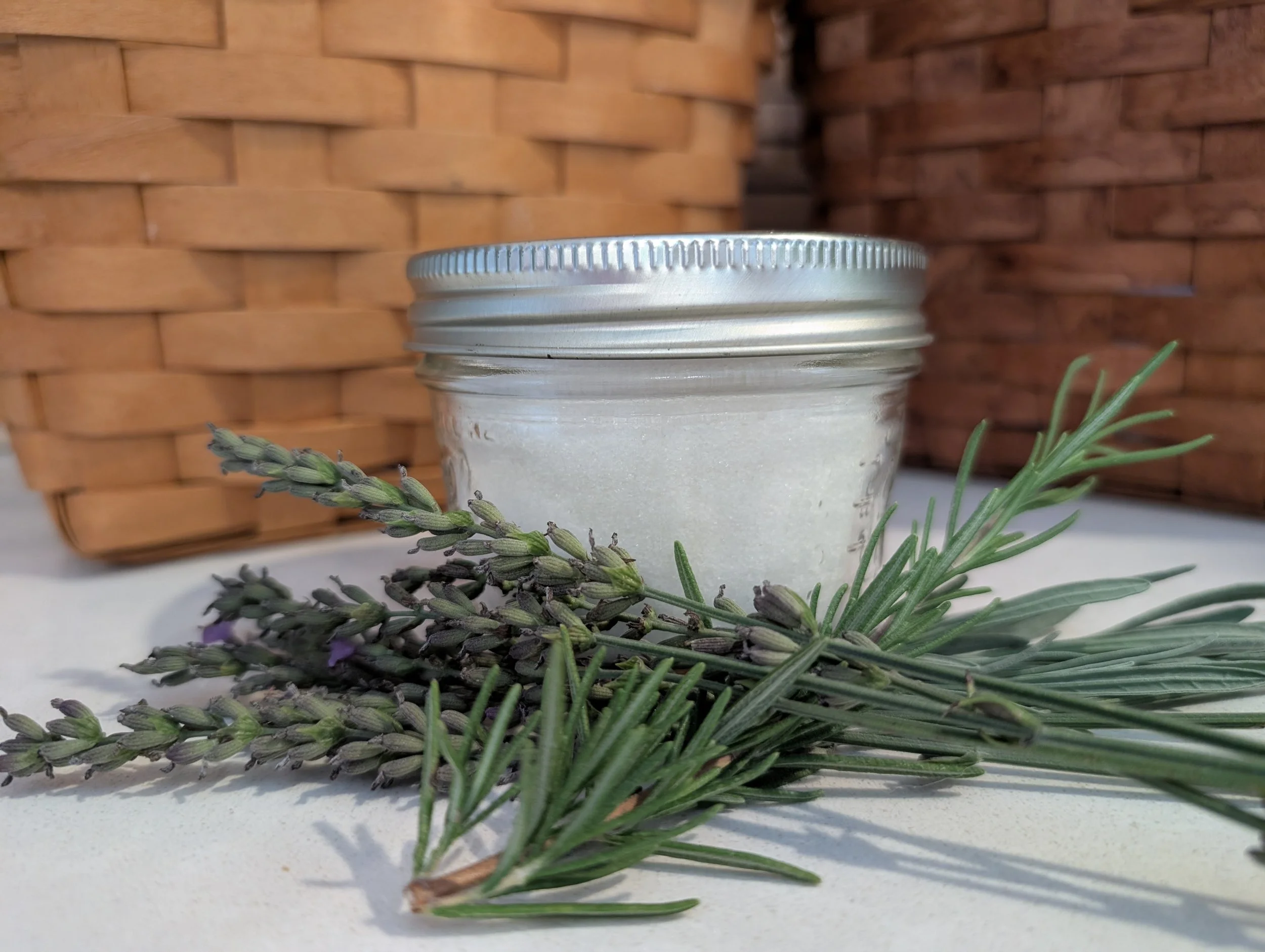  A candle in front of a woven basket, fronted by rosemary branches. 